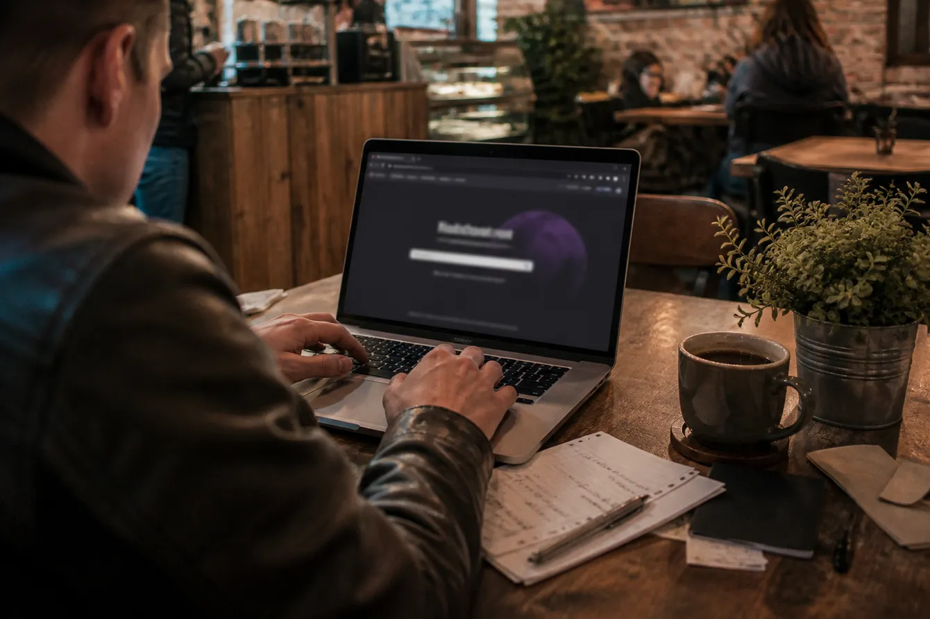 A person engaged in dark web research at a coffee shop, surrounded by notes and a laptop.